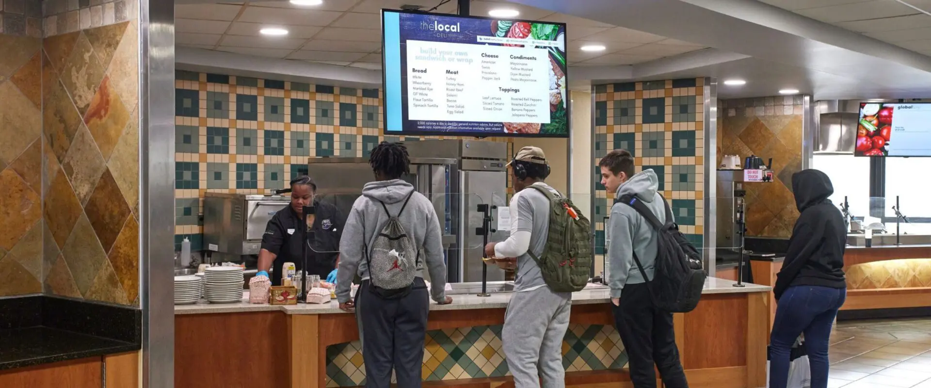 Image of students waiting in line to receive a meal at a Deli Station